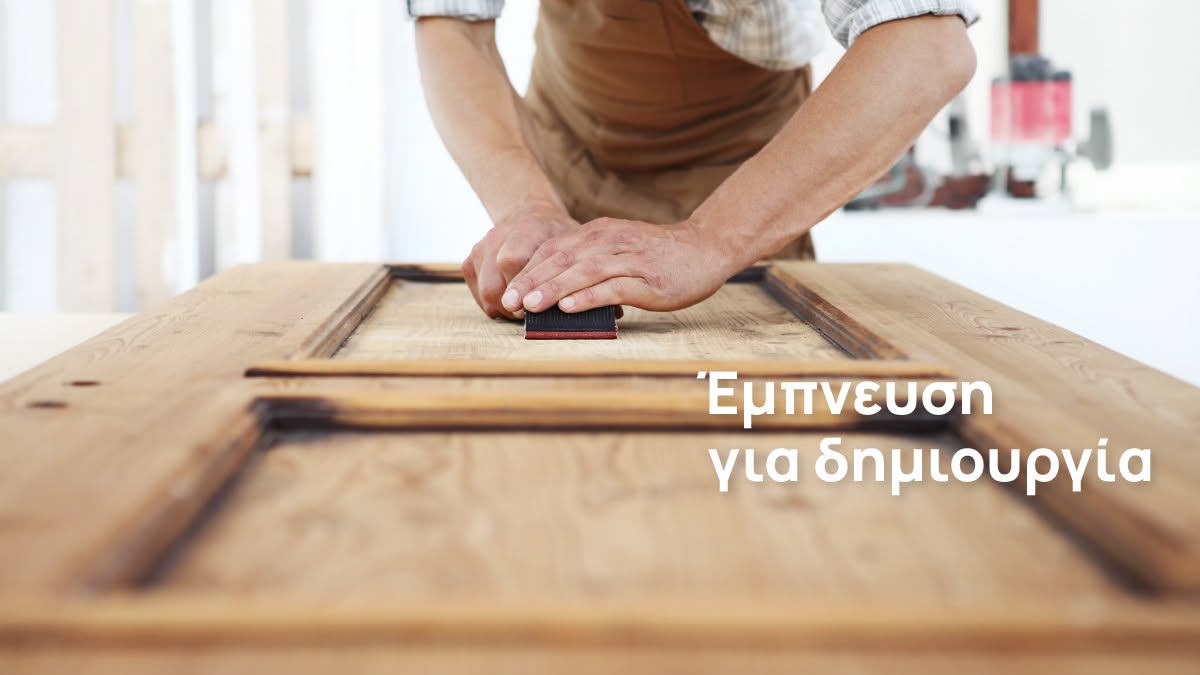 Home & Wood — hands sanding a wooden door frame in a workshop, under the phrase Έμπνευση για δημιουργία